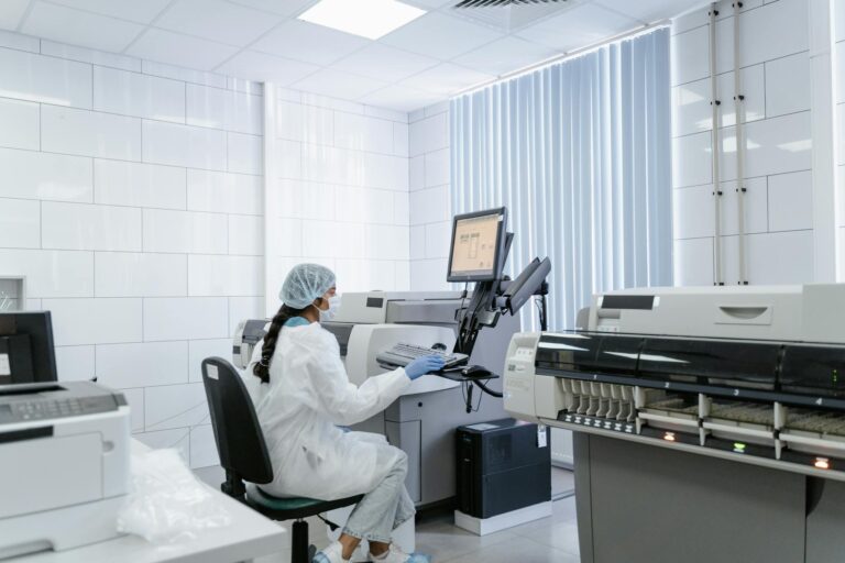 A laboratory technician wearing protective gear operates medical equipment in a sterile lab environment.
